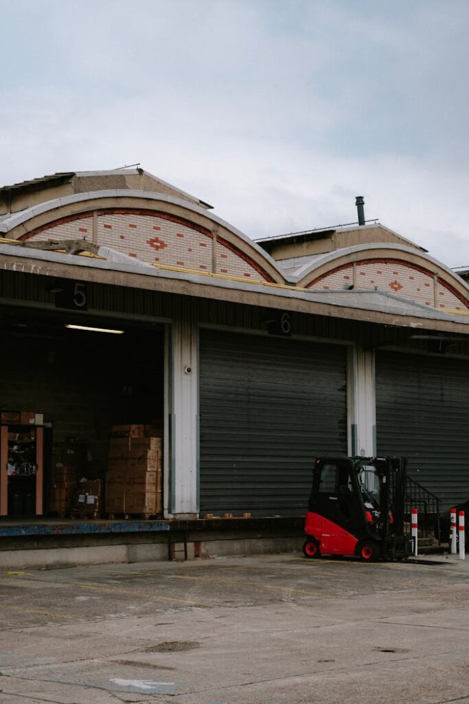 A red forklift parked at a warehouse loading dock with closed garage doors.
