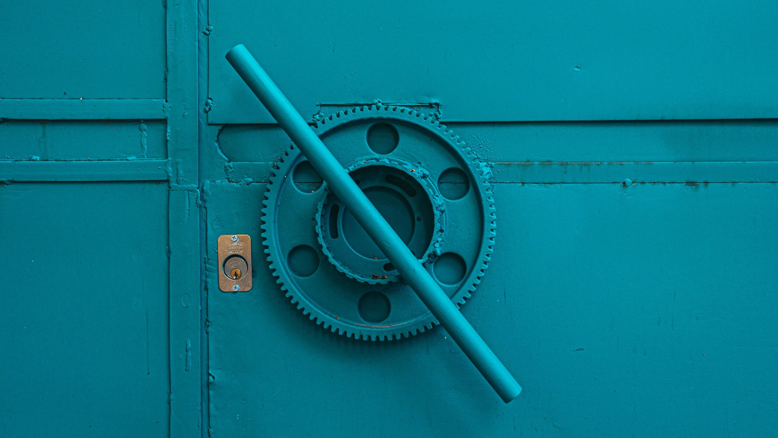 Close-up of a teal metal door with industrial gear mechanism, showcasing intricate machinery details.